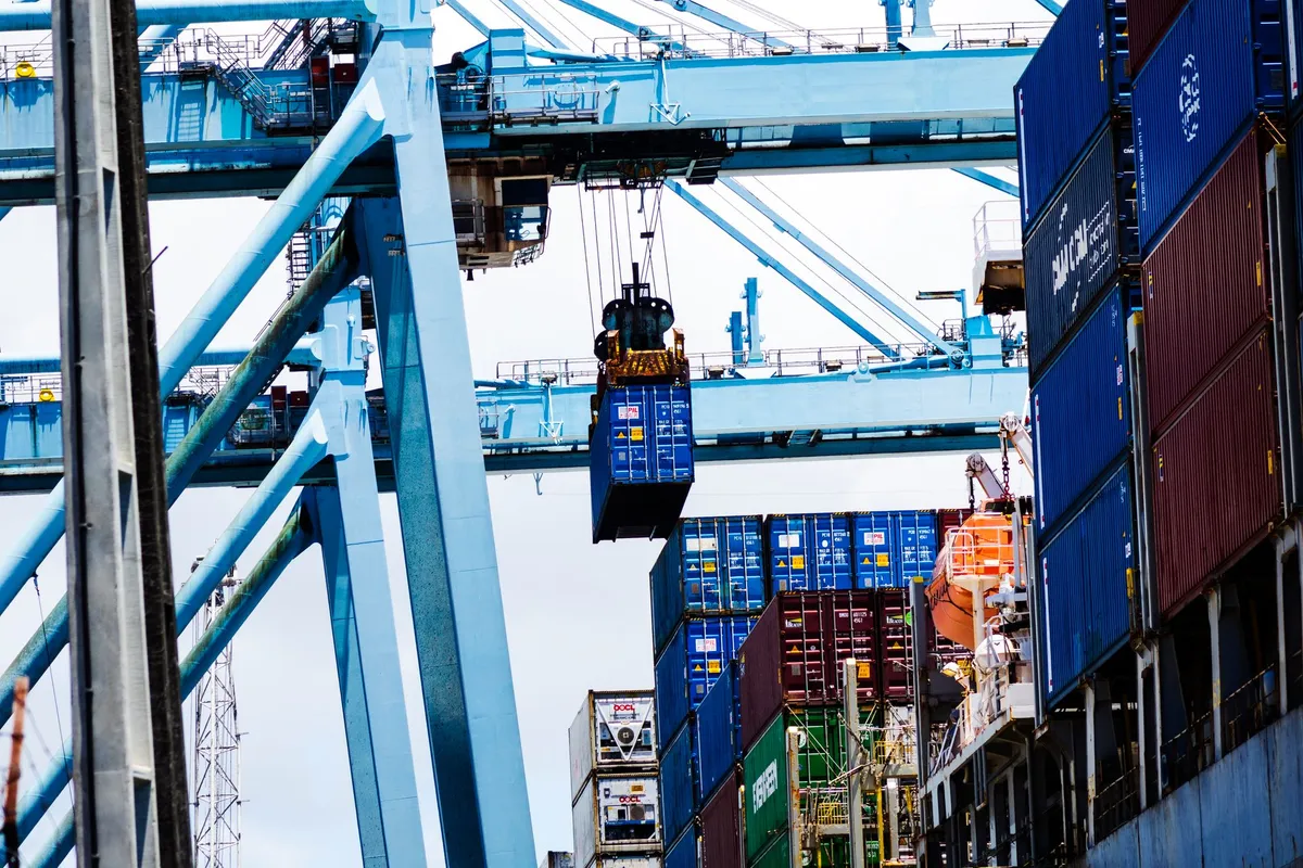Grúa pórtico de puerto suspendiendo un contenedor sobre las pilas de un buque portacontenedores.