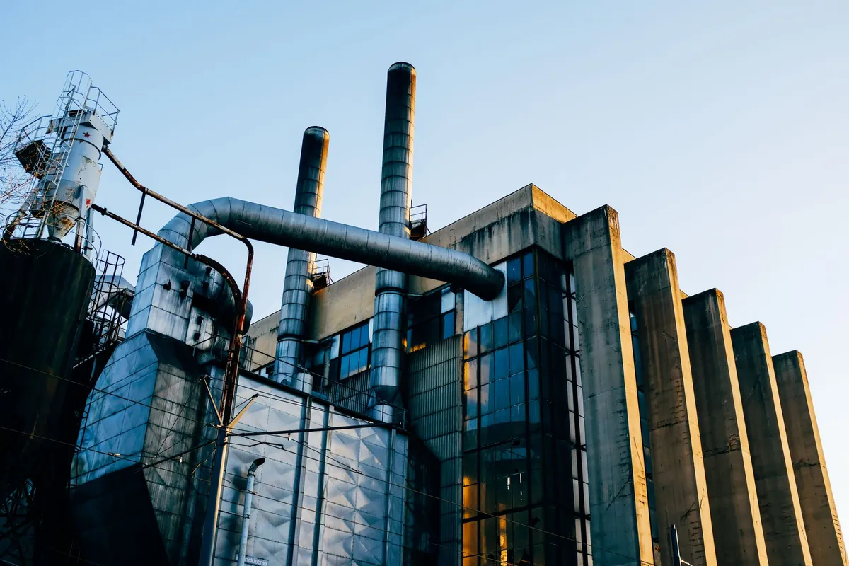 Fachada de una planta industrial vista desde abajo, con chimeneas y ductos de extracción a contraluz.